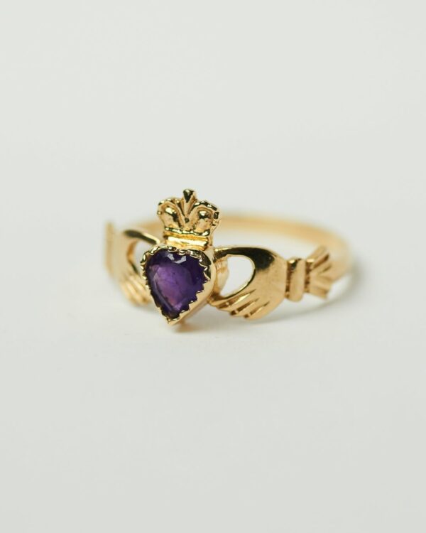 Gold ring with hands holding purple stone
